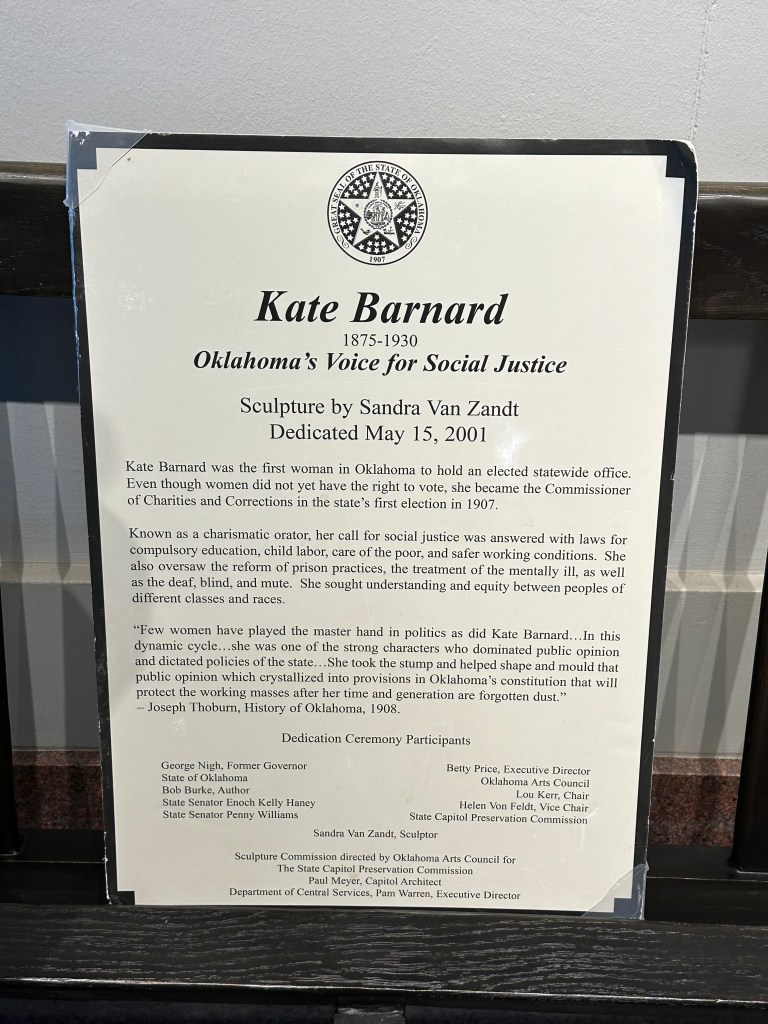Plaque honoring Kate Barnard, Oklahoma's first woman elected to office, detailing her contributions to social justice and the dedication of her sculpture by Sandra Van Zandt on May 15, 2001.