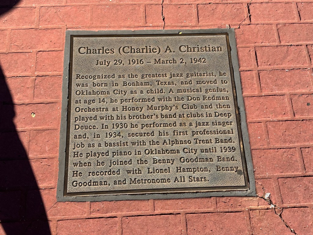 Historic plaque commemorating Charles A. Christian, a renowned jazz guitarist, located on a brick sidewalk. The plaque details his early life, musical career, and significant contributions to jazz music.