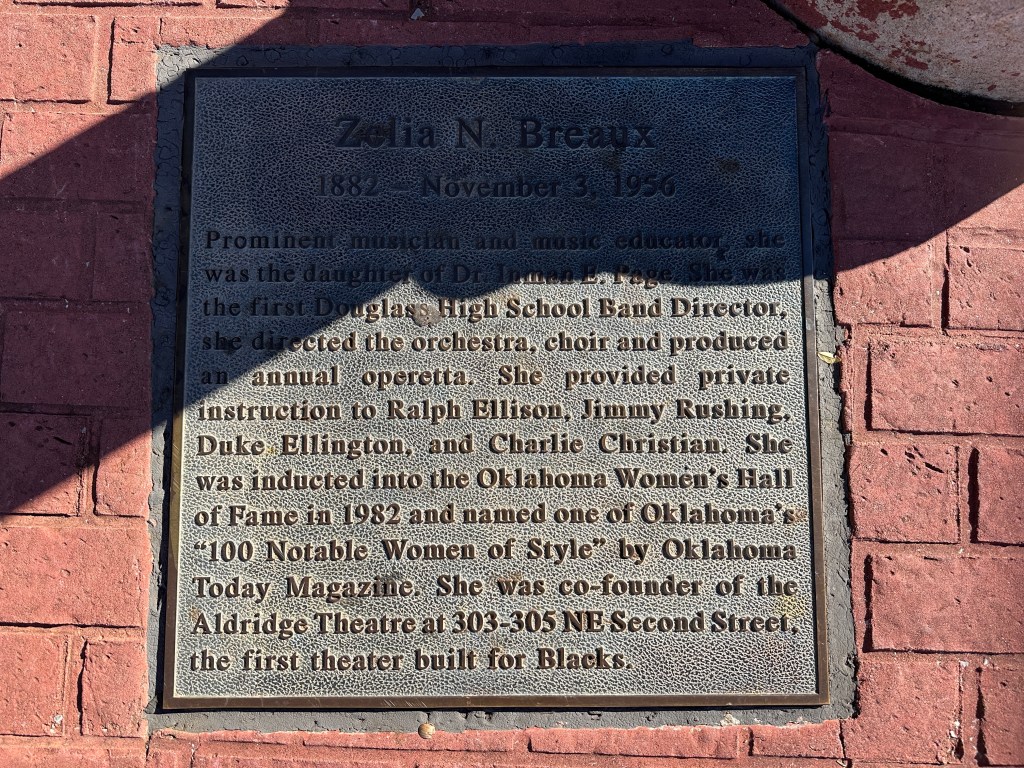 Historic plaque honoring Zelia N. Breaux, a prominent musician and music educator from Oklahoma, located on a red brick sidewalk.