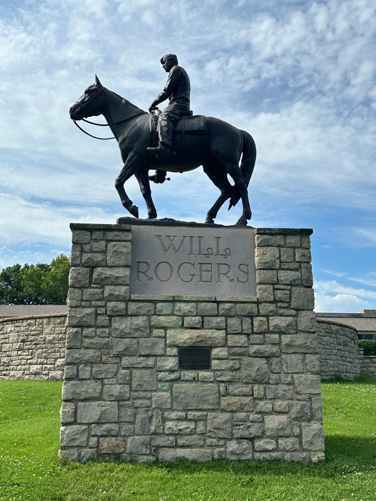 Bronze statue of Will Rogers riding a horse, displayed on a stone pedestal with his name inscribed.