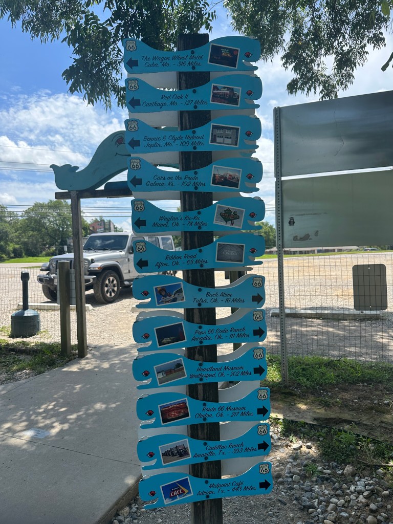 A signpost displaying various Route 66 landmarks, including distances to locations such as the Wagon Wheel Motel in Cuba, Missouri, and the Route 66 Museum in Clinton, Oklahoma.
