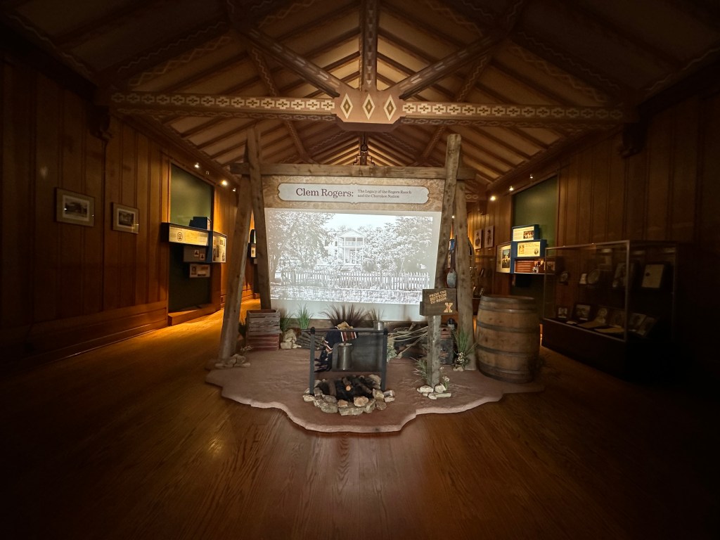 Interior view of the Will Rogers Memorial Museum featuring a display about Clem Rogers with a historical photograph, wooden paneling, and exhibits on either side.