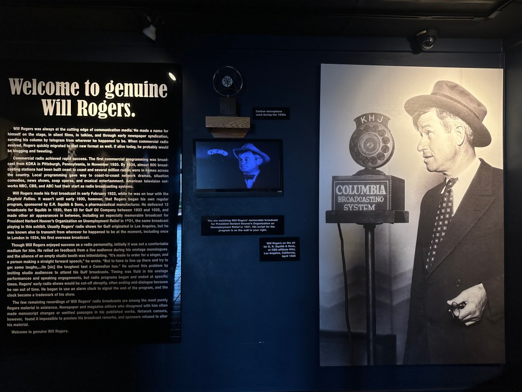 An exhibit wall featuring a welcome message about Will Rogers, with historical information on his communication career and an image of him standing next to a microphone labeled 'Columbia Broadcasting System'.
