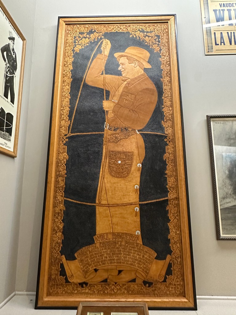A detailed leather artwork of Will Rogers, depicted holding a rope, displayed in a museum setting.