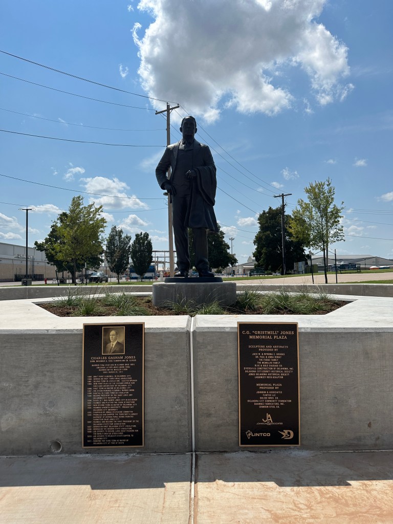 A statue of Charles G. Jones in a plaza, with plaques on either side detailing his accomplishments and contributions.
