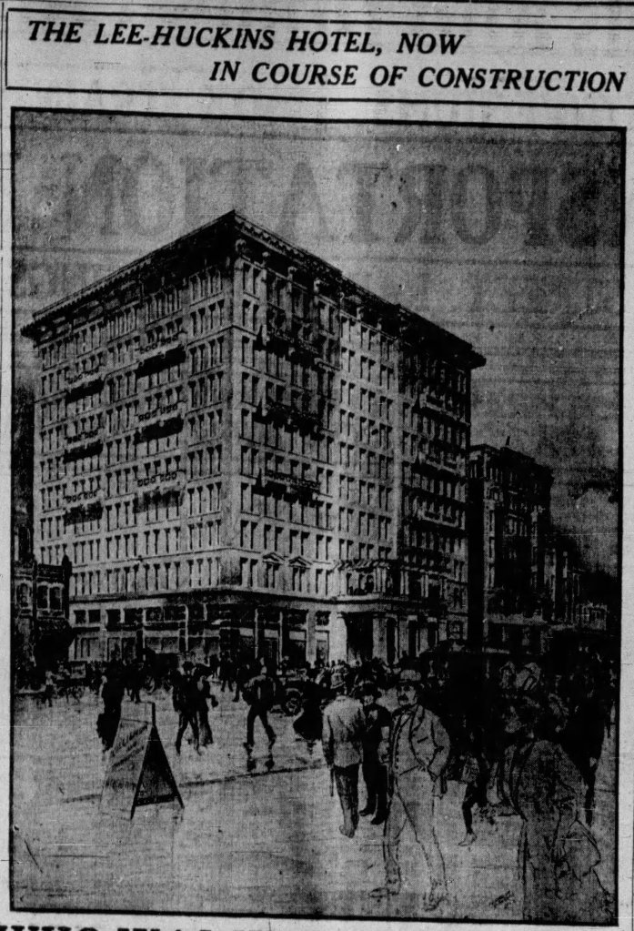 Black and white image of the Lee-Huckins Hotel during its construction, showing the building facade and a bustling street scene with people walking and storefronts visible.