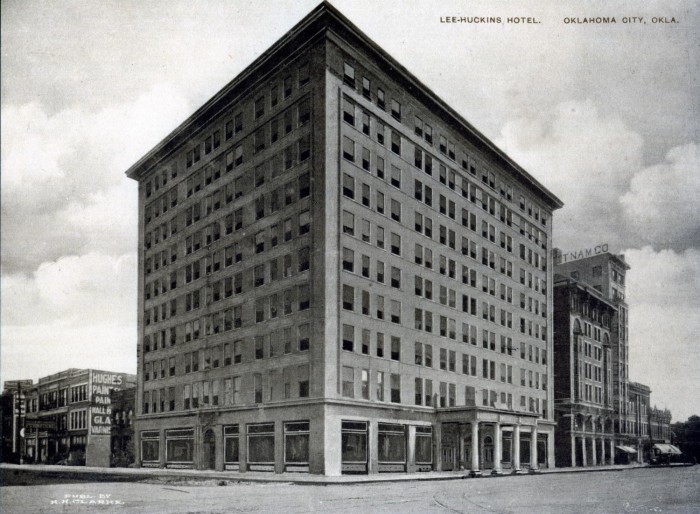 Historic Lee-Huckins Hotel in Oklahoma City, featuring a corner view of the five-story brick building with multiple windows and a neighboring building in the background.
