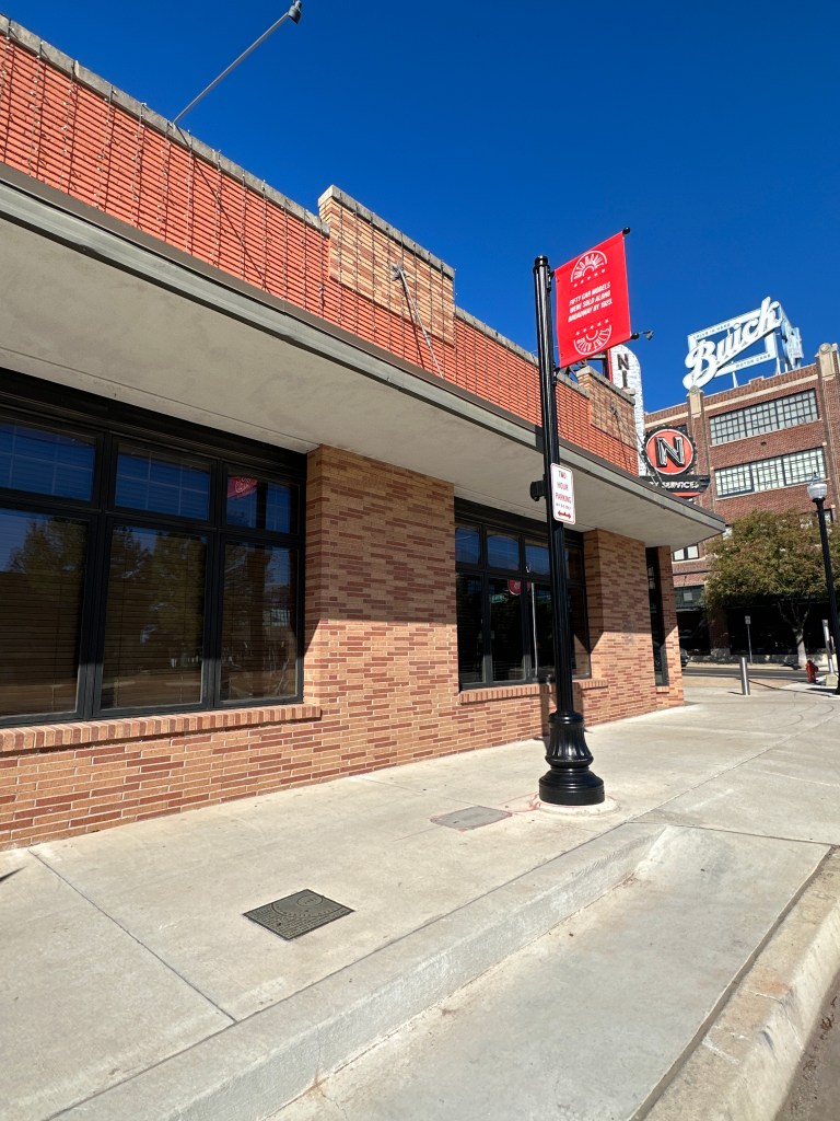 A view of a brick building in the Automobile Alley Historic District, featuring large windows, a street lamp, and a historic marker plaque on the sidewalk.