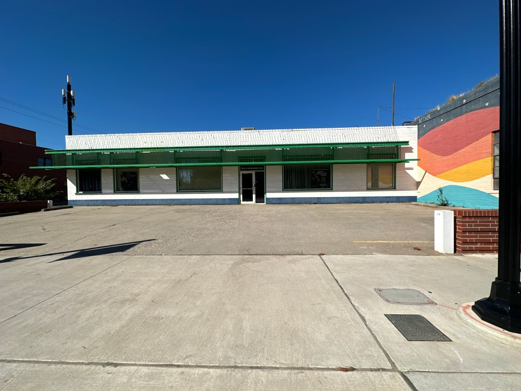 A low building with a flat roof and green accents, situated in Automobile Alley, Oklahoma City, with a clear blue sky in the background.