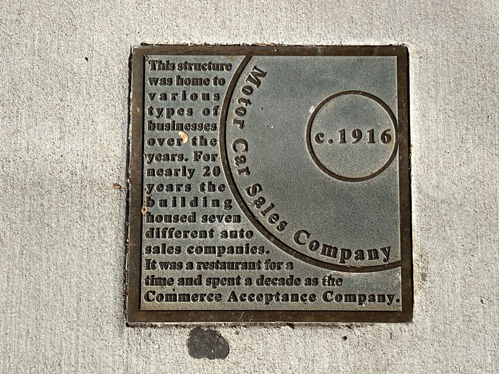Historic marker plaque for the Motor Car Sales Company, detailing its history and significance, located on the sidewalk.
