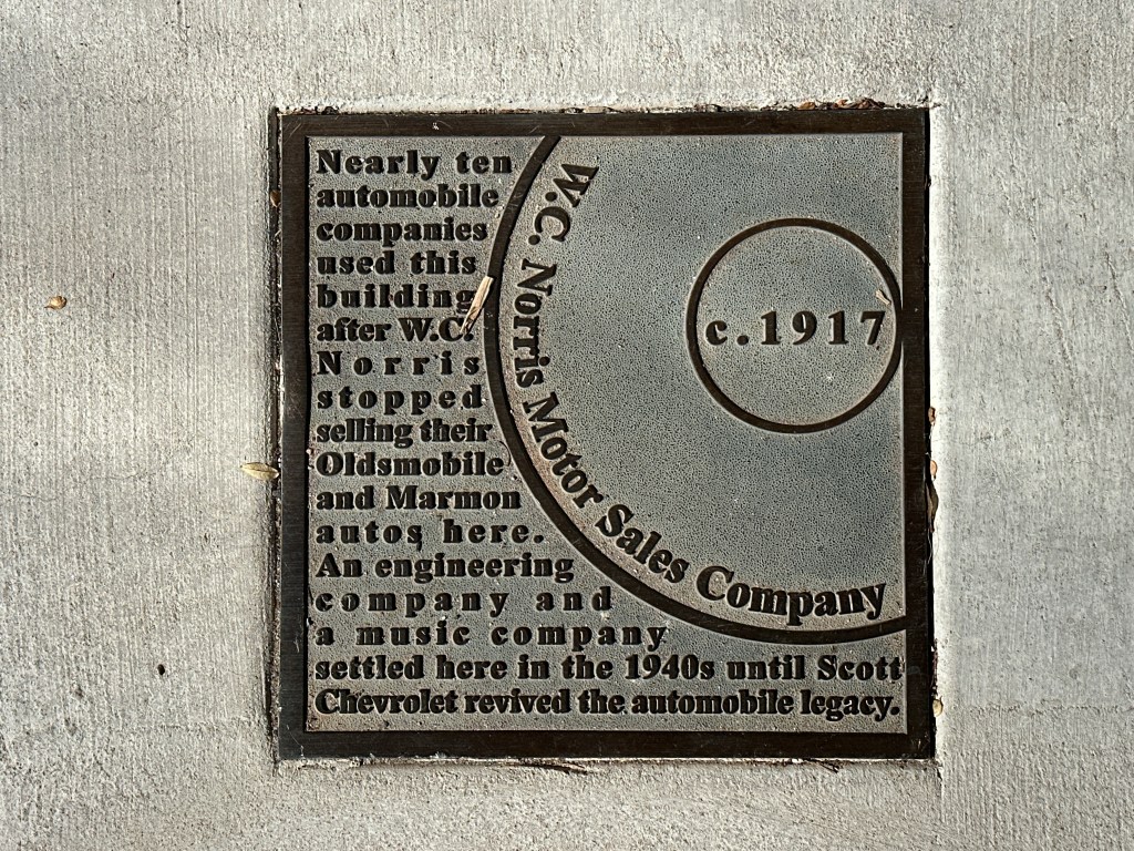 Close-up of a historic marker plaque for W.C. Norris Motor Sales Company, detailing its history and use by multiple automobile companies around 1917.