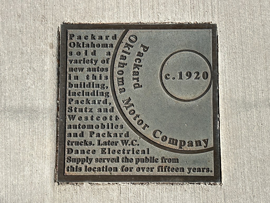 Historic marker plaque for Packard Motor Company in Oklahoma City, detailing its history and significance, set in the sidewalk.
