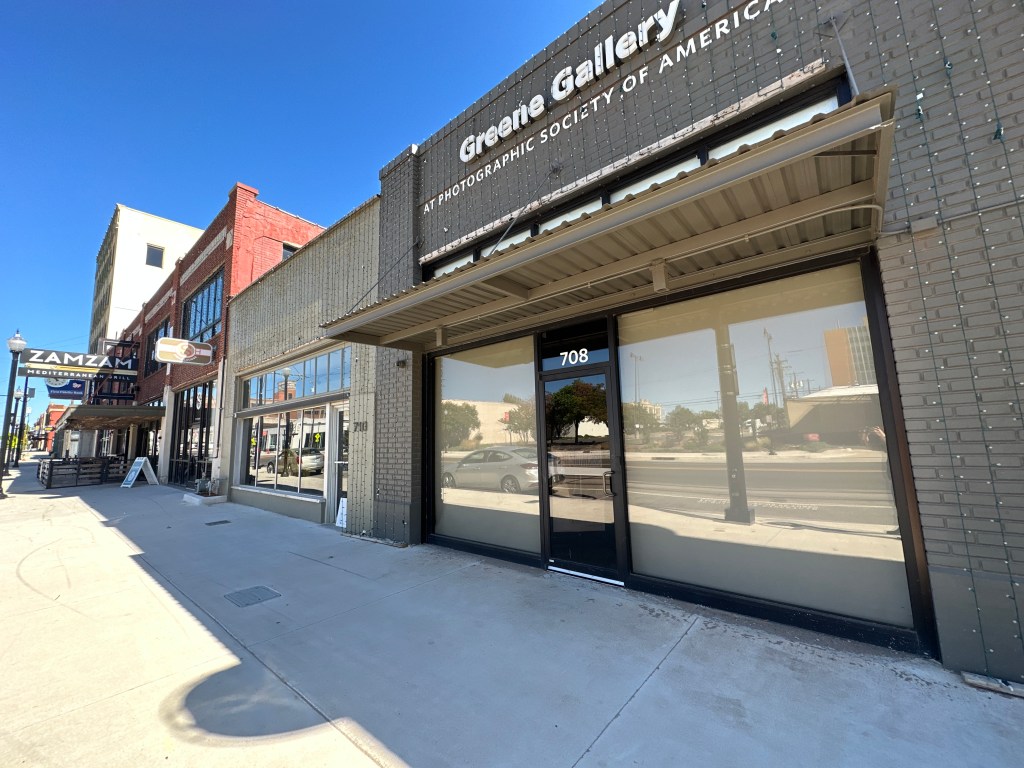 Street view of Greene Gallery, a building featuring large windows and a sign indicating it is part of the Photographic Society of America, located at 708 Broadway in Automobile Alley, Oklahoma City.