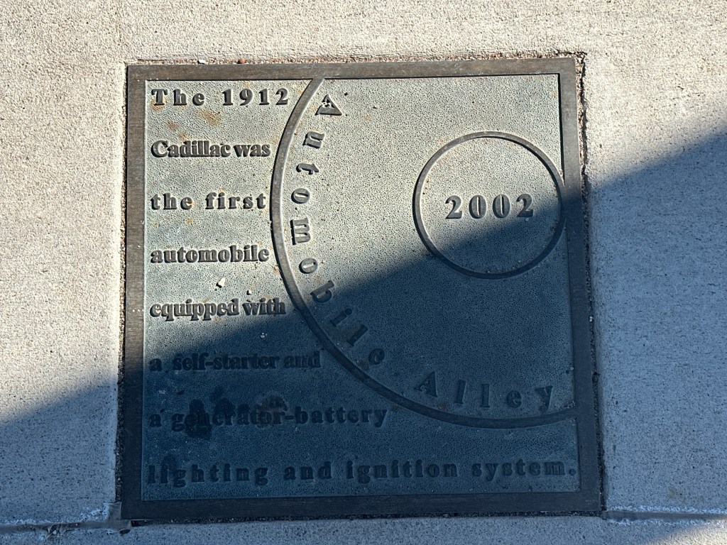 Historic marker plaque commemorating the 1912 Cadillac as the first automobile equipped with a self-starter and generator-battery lighting system, located in Automobile Alley.