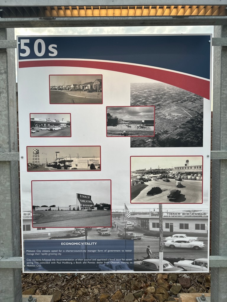 A sign displaying historical photographs from the 1950s, showcasing buildings, streets, and local businesses in Midwest City.