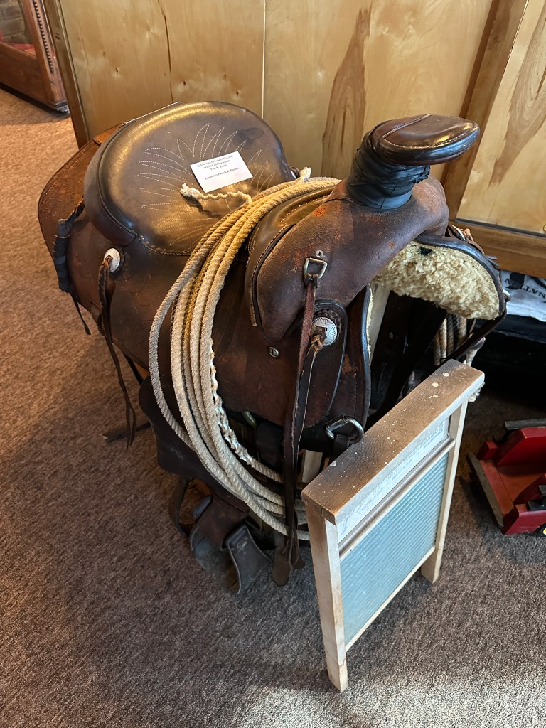 A vintage saddle with ropes and a washboard displayed in a museum setting.