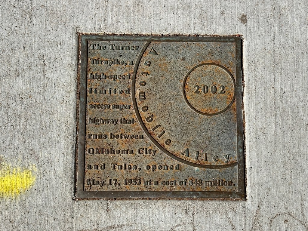 A historic marker plaque embedded in the sidewalk, detailing the Turner Turnpike, a high-speed highway that connects Oklahoma City and Tulsa, opened in 1953.