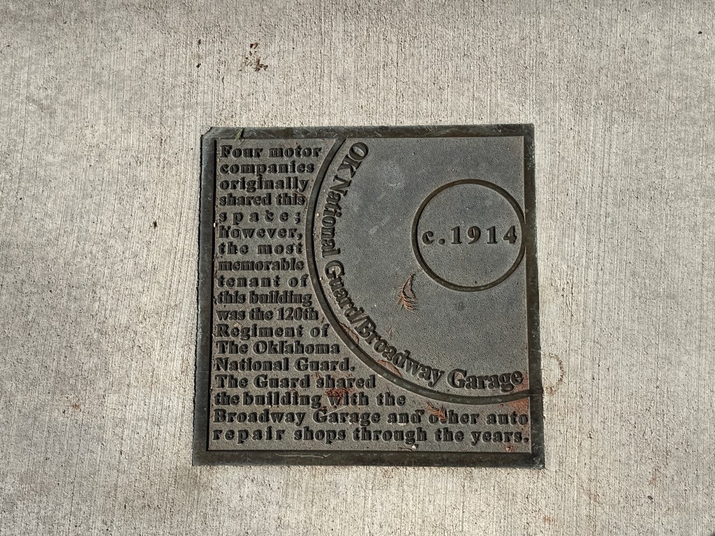 Historic marker plaque describing the OK National Guard and Broadway Garage from around 1914, set in the sidewalk of Automobile Alley.