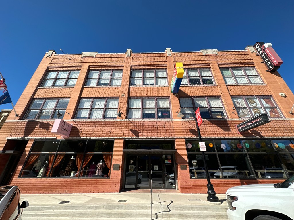 Front view of a historic brick building in Automobile Alley, Oklahoma City, featuring large windows, decorative signage, and flags.