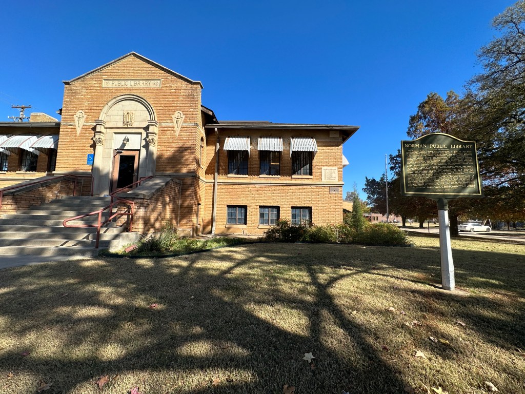 Historic building of the Norman Public Library in Oklahoma, featuring Italian Renaissance architecture, with a historic marker in front.