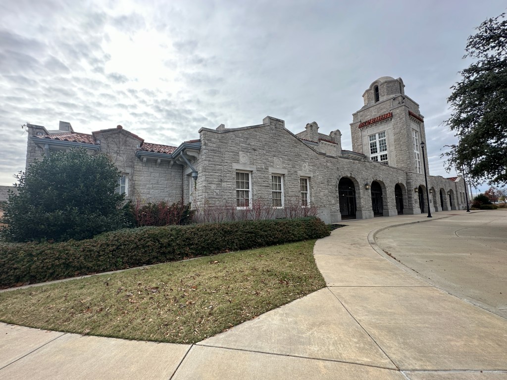 Exterior view of the historic Union Station in Oklahoma City, showcasing its Bedford stone architecture and decorative roof details against a cloudy sky.