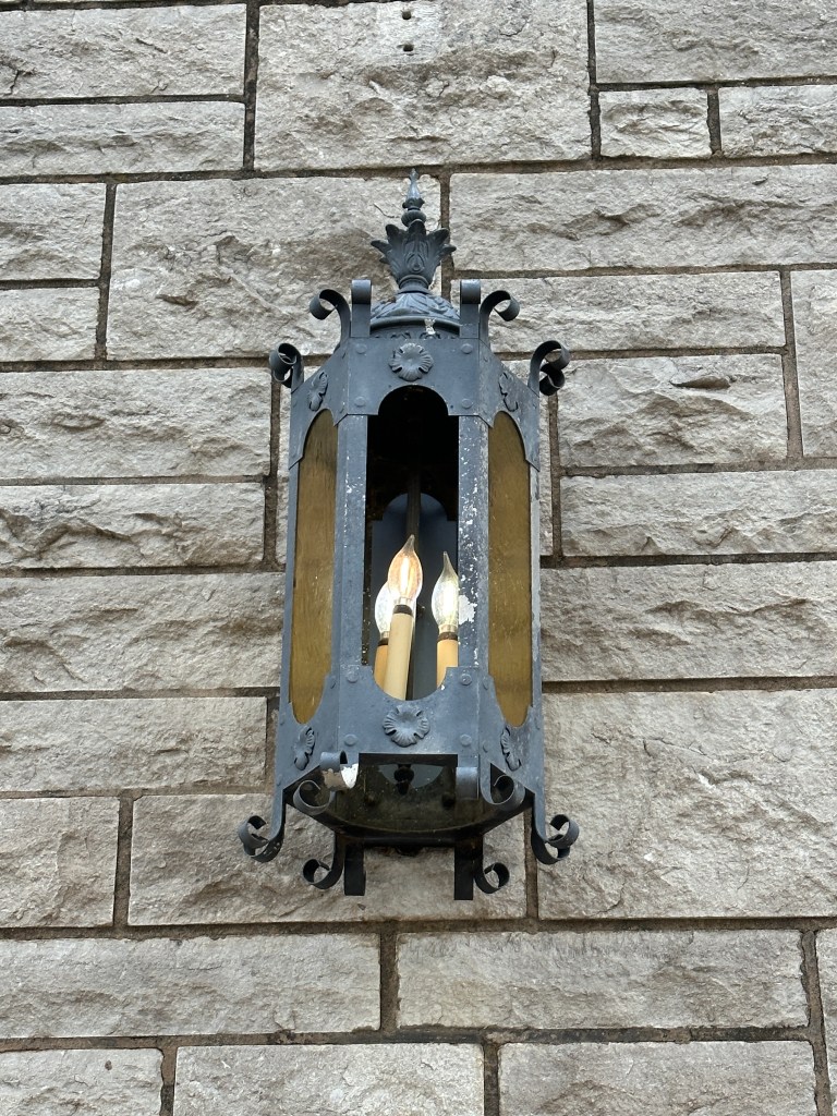 A decorative lantern mounted on a stone wall, featuring a vintage design with three candle-like bulbs.