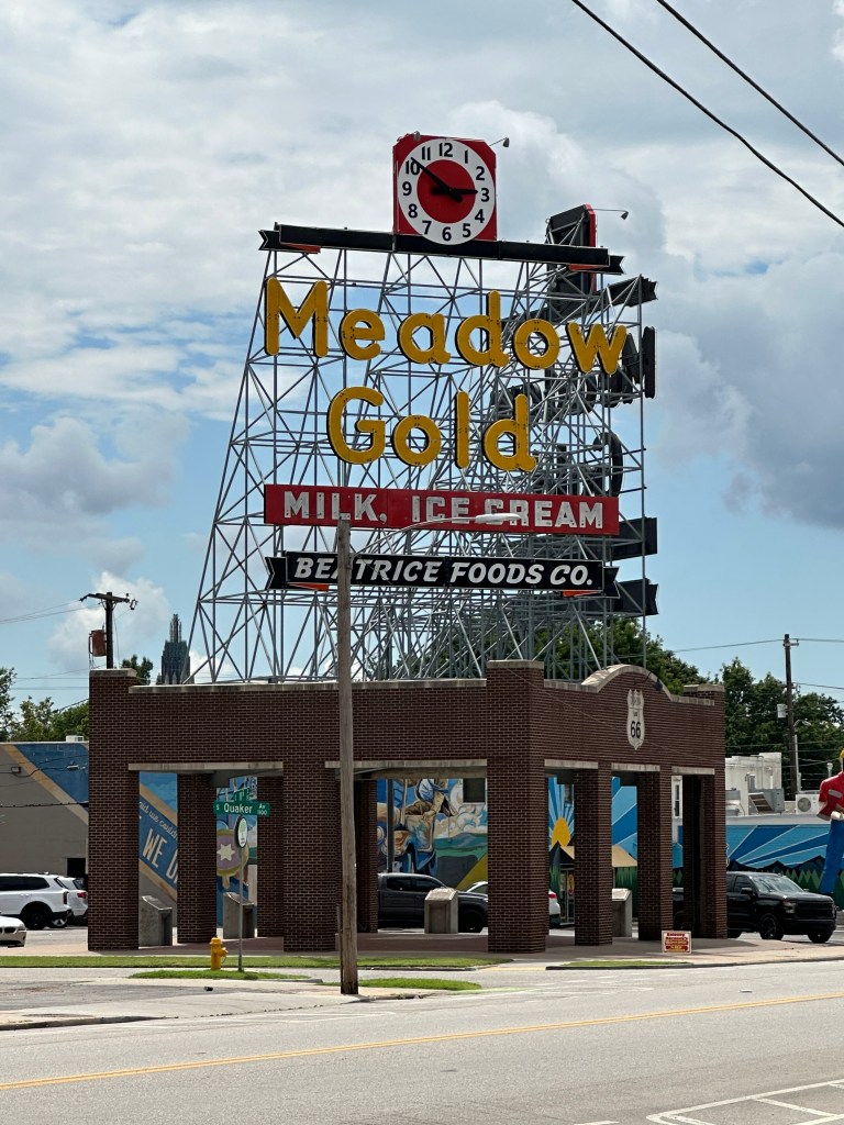 Historic Meadow Gold neon sign in Tulsa, Oklahoma, featuring yellow lettering and a clock, mounted on a brick pavilion.
