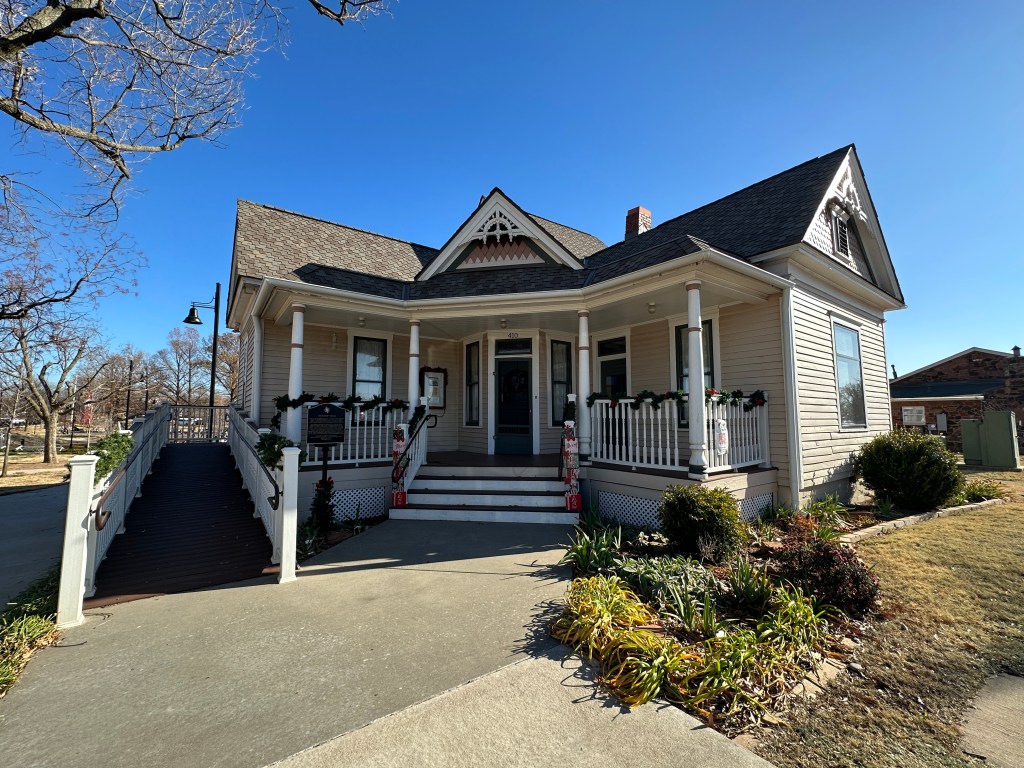 Front view of the Rodkey House, a Victorian style home in Edmond, Oklahoma, featuring a porch, decorative architecture, and surrounding landscaping.