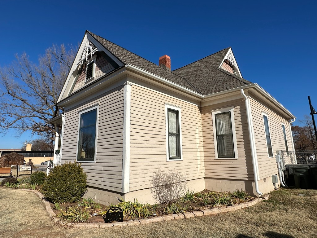 Side view of the Rodkey House, a restored Victorian home in Edmond, Oklahoma, showcasing pale peach exterior and architectural details.