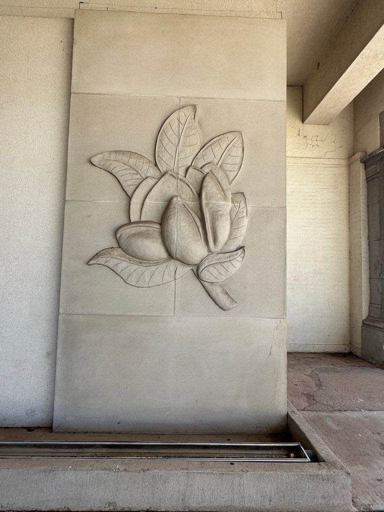 Relief sculpture of a magnolia flower on a stone wall, featuring detailed leaves and petals.