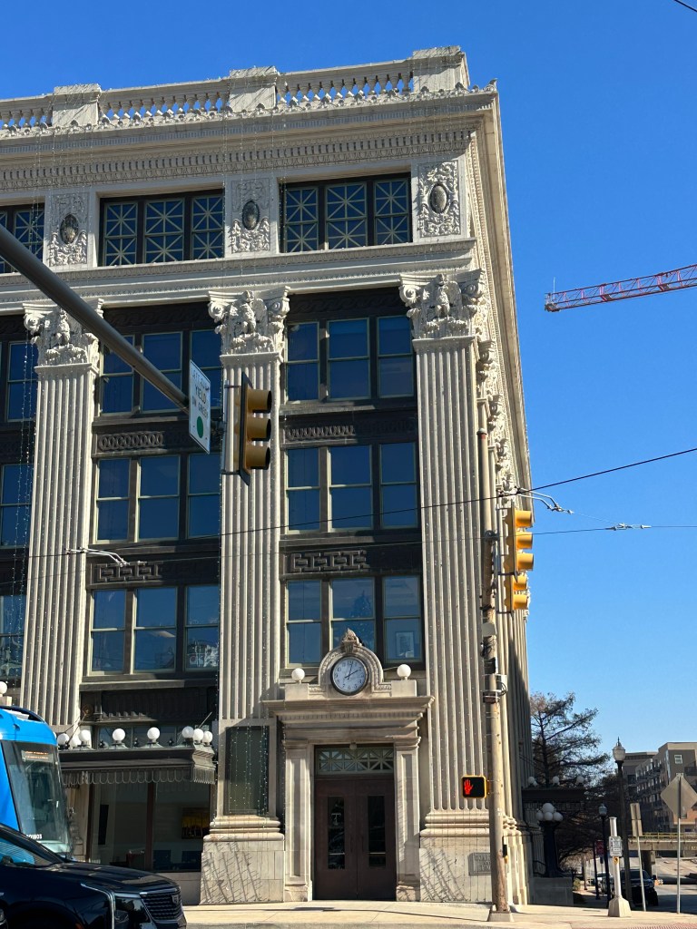 Historic building with ornate architectural details, including columns and decorative elements, featuring large windows and a clock above the entrance.