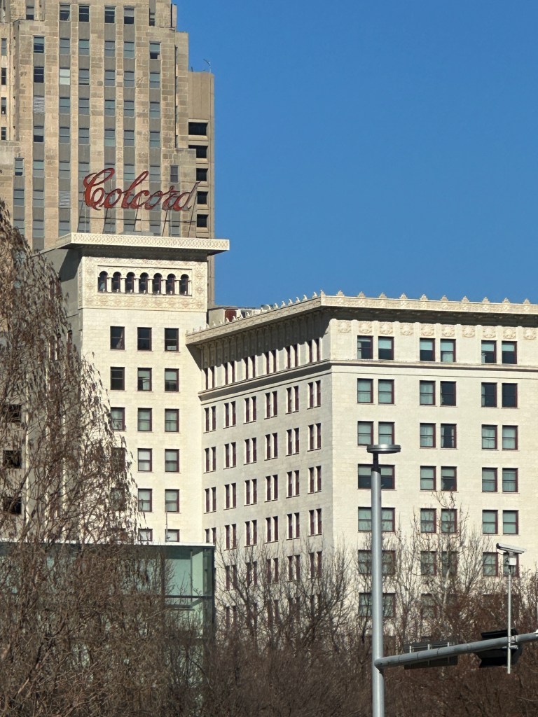 Historic buildings featuring architectural details against a clear blue sky, with a prominent red 'Colcord' sign on top of one structure.
