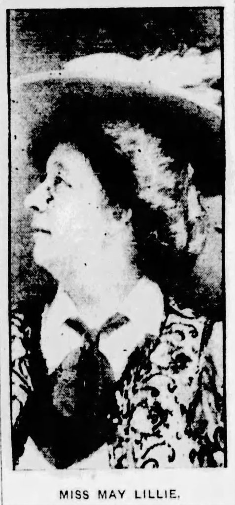 Profile portrait of a woman named Miss May Lillie, wearing a large hat and an ornate outfit, looking upward.
