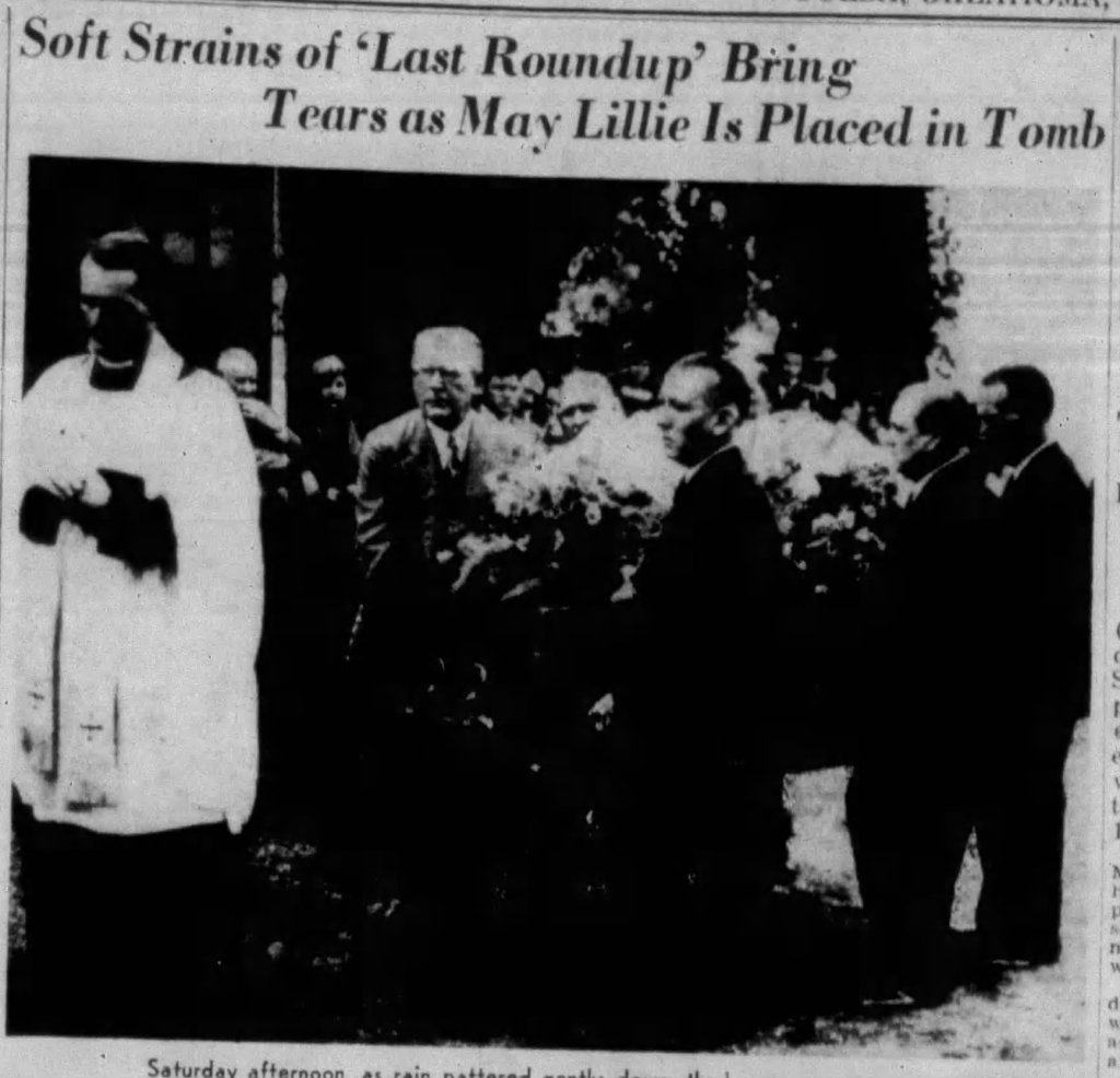 A group of mourners gathered at a gravesite as a clergyman officiates the burial service for May Lillie, with floral arrangements visible.