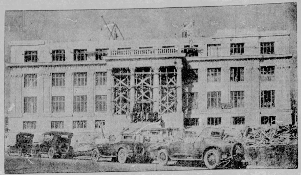 Historic building under renovation with scaffolding, surrounded by vintage cars and construction debris.