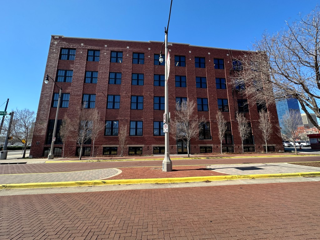 Front view of a brick building with multiple windows, surrounded by barren trees and a clear blue sky.