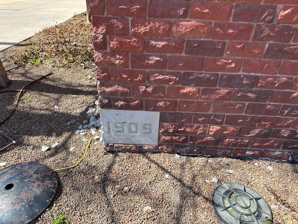 A close-up view of a brick wall with a stone plaque displaying the year '1909' near the base.