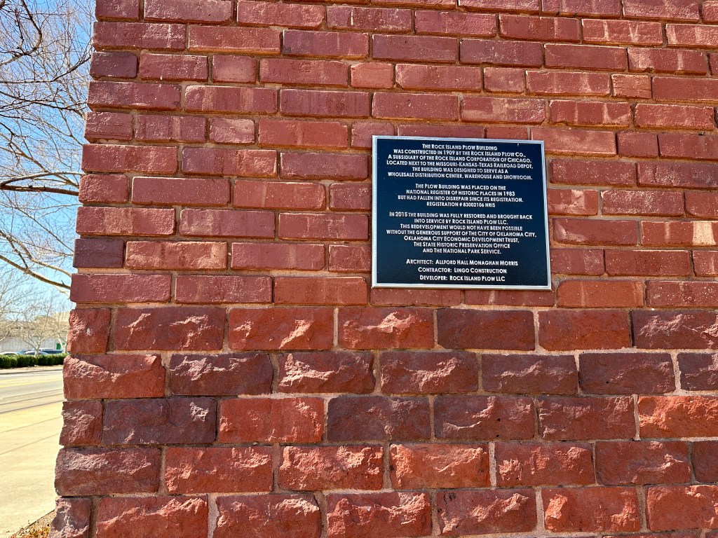 A brick wall featuring a historical plaque about the Rock Island Plow Building, detailing its construction history, significance, and restoration efforts.