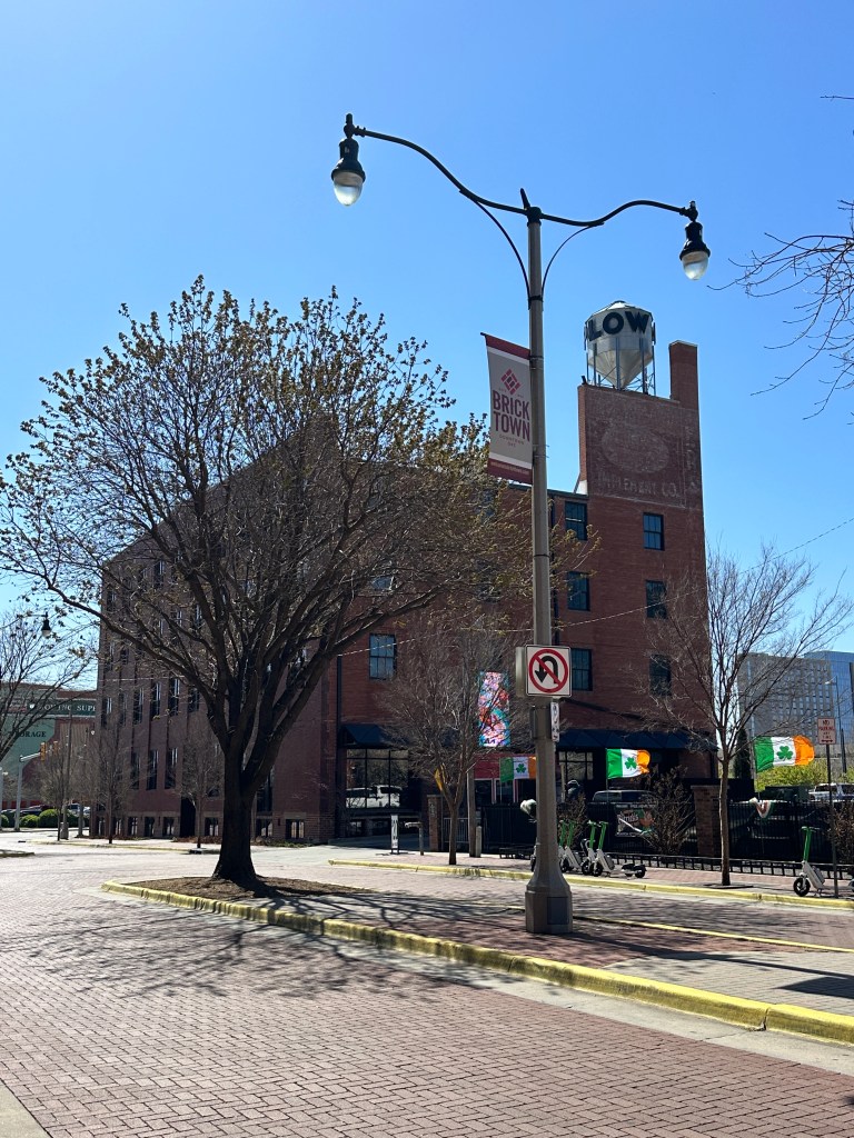 View of a brick building in Bricktown with street lamps and trees in the foreground, blue sky overhead.