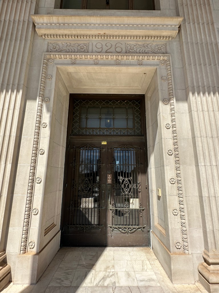 Entrance with ornate double doors, featuring decorative metal grilles and the year '1926' engraved above.